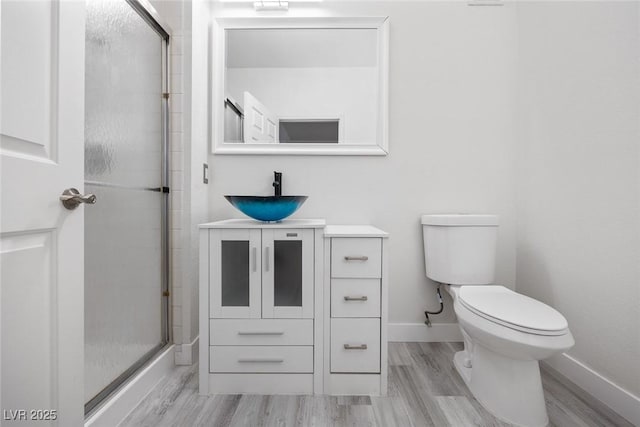 bathroom with toilet, a shower with shower door, vanity, wood finished floors, and baseboards