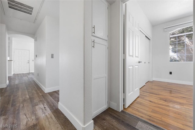 hallway with visible vents, arched walkways, baseboards, and dark wood finished floors
