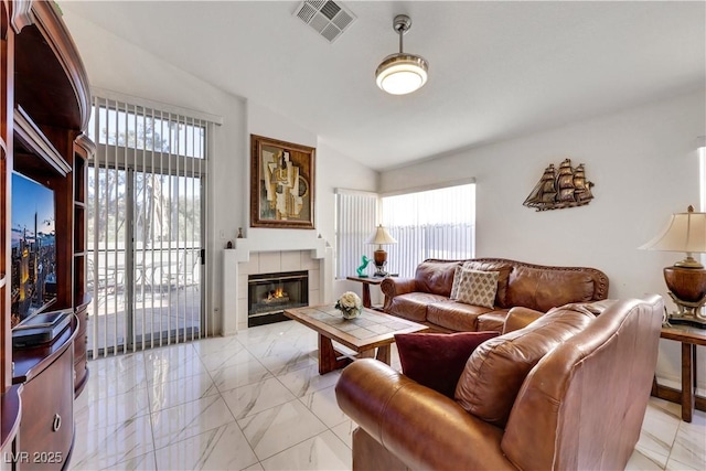 living room with vaulted ceiling, a tiled fireplace, and visible vents