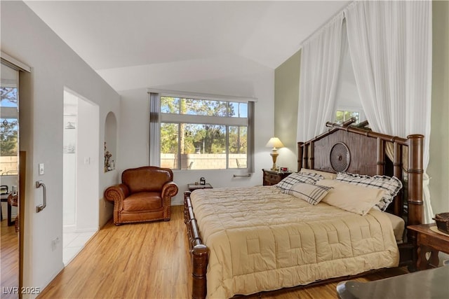 bedroom with vaulted ceiling, arched walkways, and wood finished floors