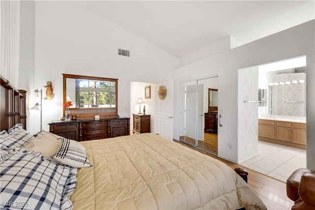 bedroom featuring a closet, visible vents, ensuite bathroom, high vaulted ceiling, and light wood-type flooring