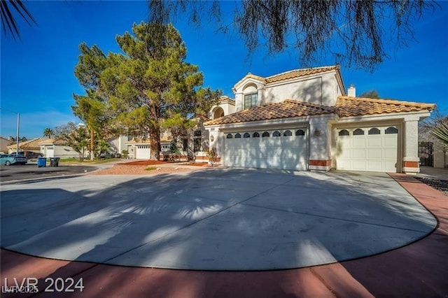 mediterranean / spanish-style home featuring a garage, a tile roof, driveway, stucco siding, and a chimney