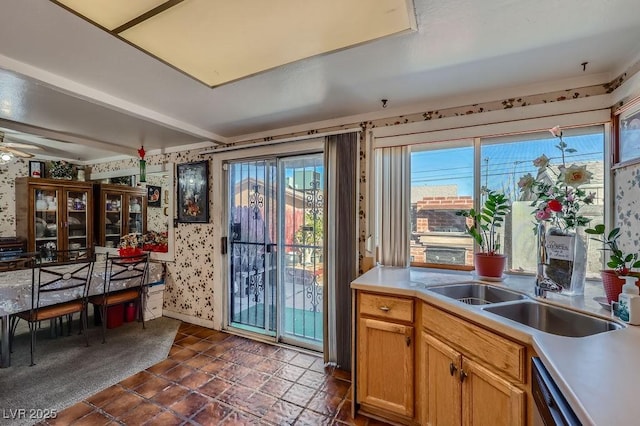 kitchen featuring wallpapered walls, dishwashing machine, light countertops, dark carpet, and a sink