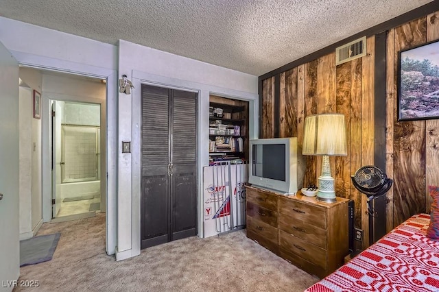 bedroom with wooden walls, visible vents, a textured ceiling, and carpet flooring