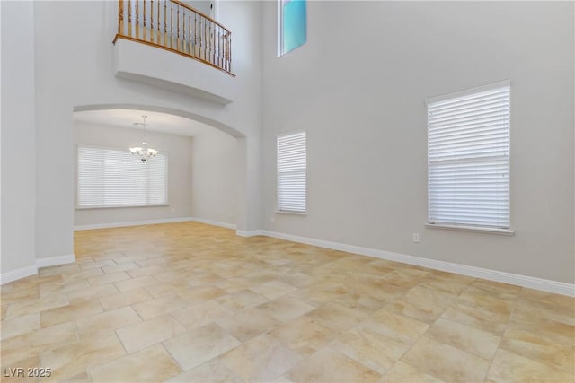 empty room featuring a chandelier, arched walkways, a towering ceiling, and baseboards