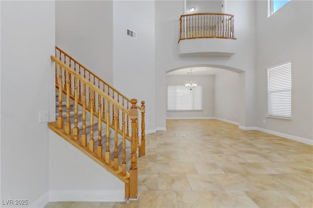 foyer featuring baseboards, a high ceiling, arched walkways, and a chandelier