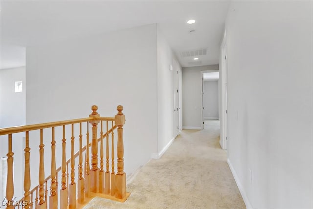 hallway with light carpet, an upstairs landing, visible vents, and baseboards