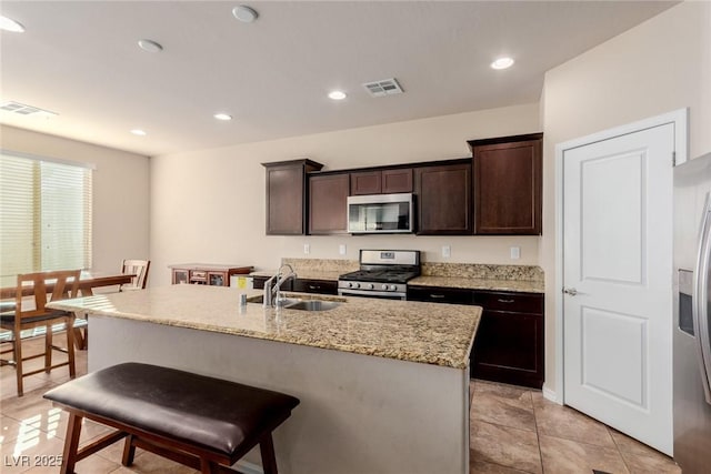 kitchen with a center island with sink, visible vents, appliances with stainless steel finishes, light stone counters, and a sink