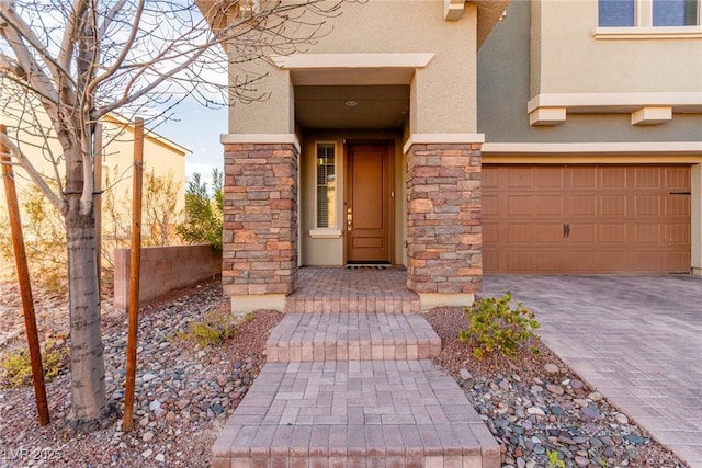 doorway to property featuring a garage, fence, stone siding, decorative driveway, and stucco siding