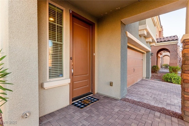 view of exterior entry featuring a garage, a tiled roof, decorative driveway, and stucco siding