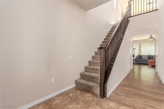 stairway with baseboards, arched walkways, a ceiling fan, and wood finished floors