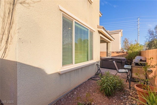 view of side of property featuring a patio area, stucco siding, a fenced backyard, and a hot tub