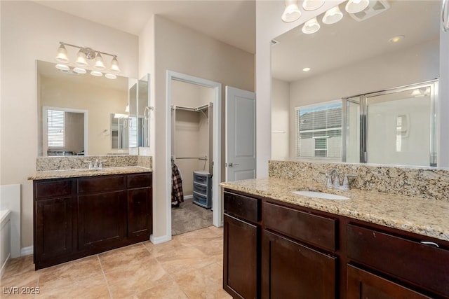 full bathroom with a stall shower, two vanities, a sink, and a walk in closet