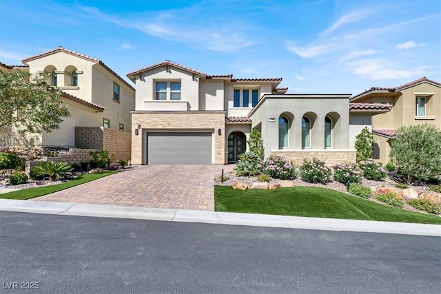 mediterranean / spanish house with stone siding, decorative driveway, an attached garage, and stucco siding