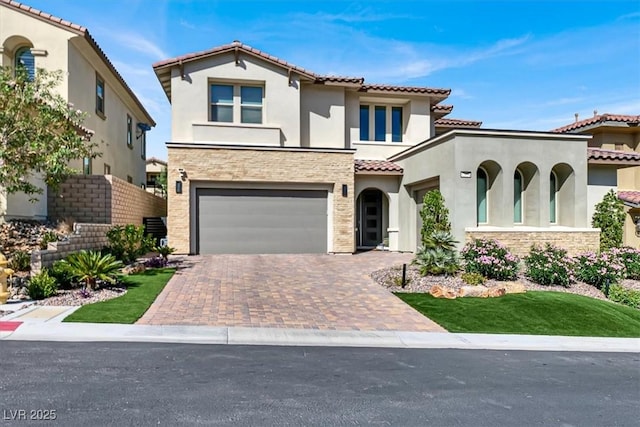 mediterranean / spanish house featuring an attached garage, a tile roof, stone siding, decorative driveway, and stucco siding