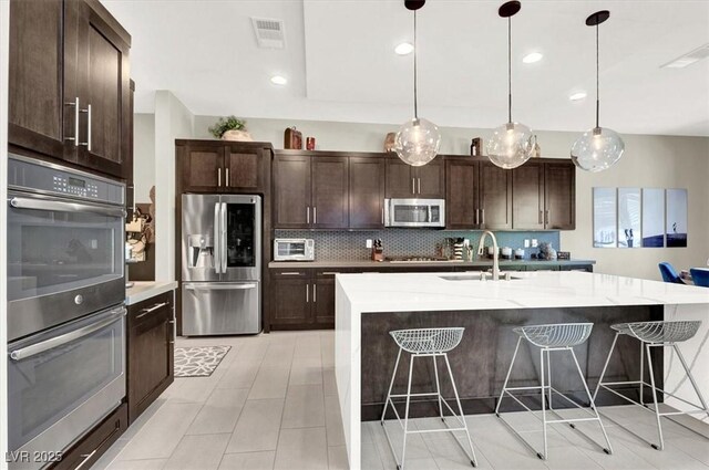 kitchen featuring stainless steel appliances, a kitchen island with sink, decorative light fixtures, and visible vents