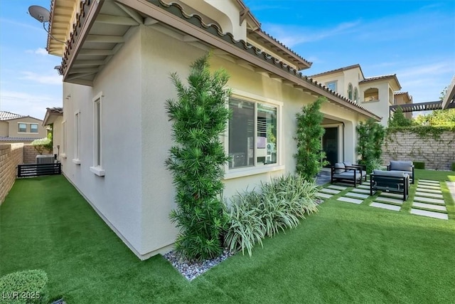 view of side of property featuring outdoor lounge area, a lawn, fence, and stucco siding