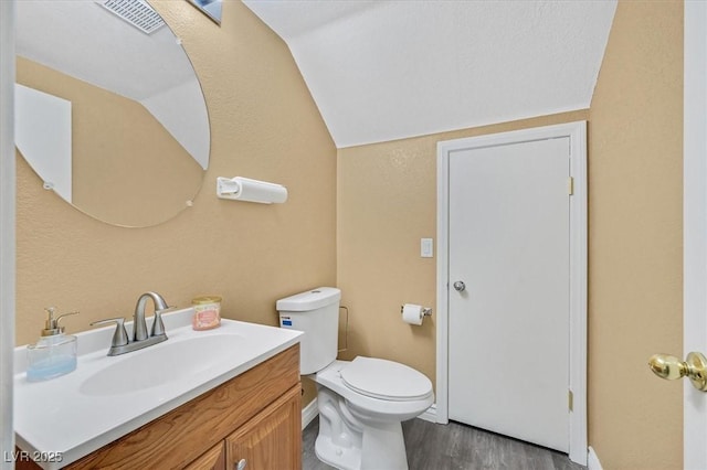 half bathroom featuring vaulted ceiling, vanity, toilet, and wood finished floors