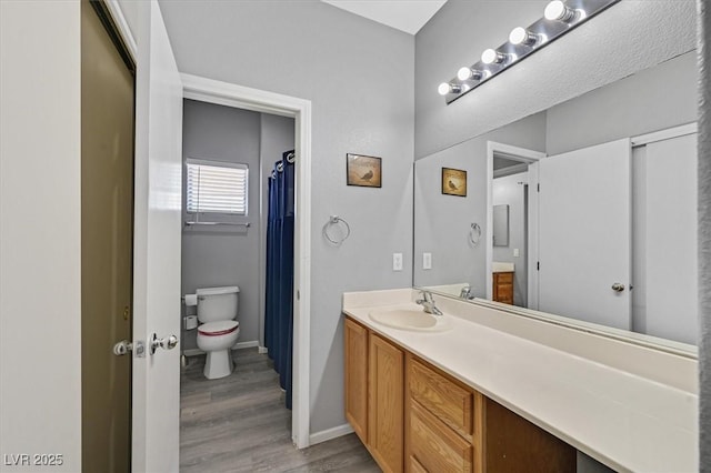 bathroom with toilet, wood finished floors, vanity, and baseboards