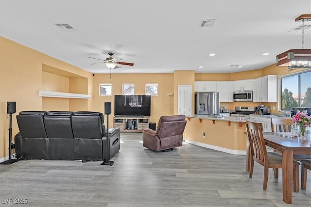 living area with recessed lighting, visible vents, a ceiling fan, light wood-type flooring, and baseboards