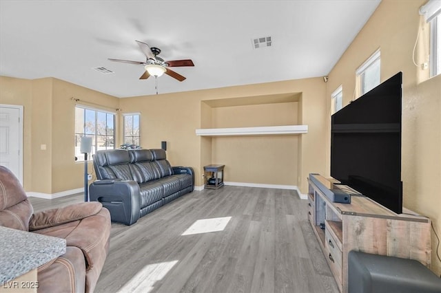 living area with baseboards, a ceiling fan, visible vents, and light wood-style floors