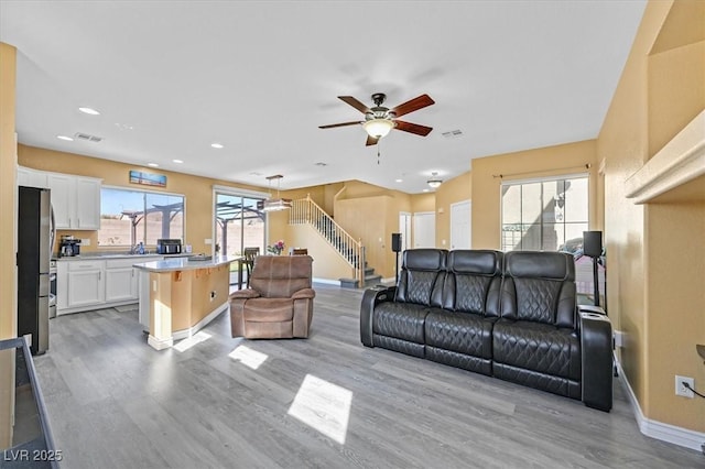 living room featuring light wood-type flooring, ceiling fan, stairs, and baseboards