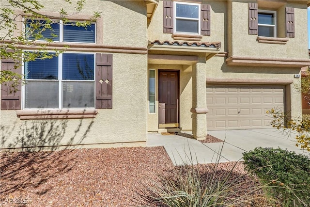 entrance to property featuring a garage, driveway, a tiled roof, and stucco siding