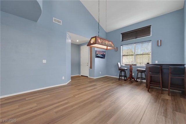 interior space with high vaulted ceiling, wood finished floors, visible vents, and baseboards