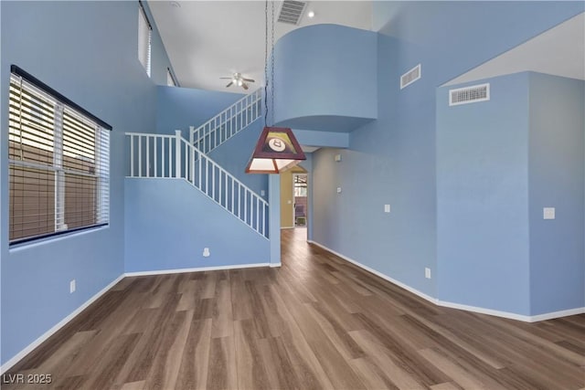 unfurnished living room with visible vents, stairway, a high ceiling, and wood finished floors