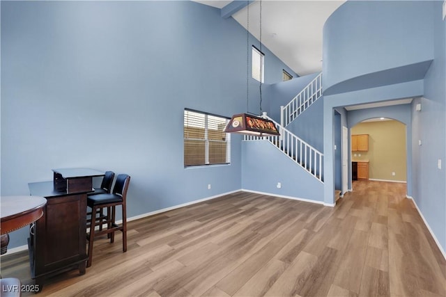 home office featuring arched walkways, beam ceiling, wood finished floors, high vaulted ceiling, and baseboards