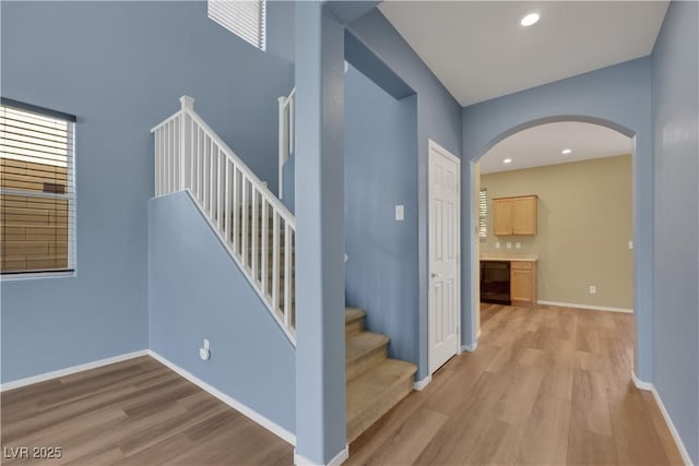 staircase with arched walkways, recessed lighting, wood finished floors, and baseboards