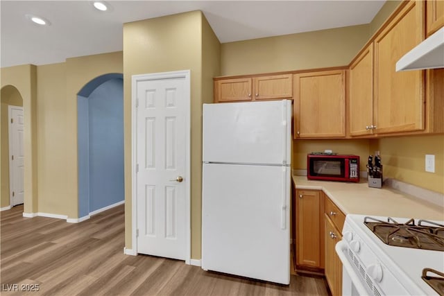 kitchen with white appliances, arched walkways, wood finished floors, light countertops, and under cabinet range hood