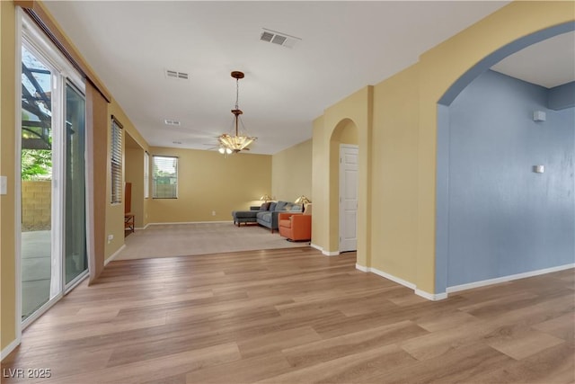 interior space featuring arched walkways, light wood-type flooring, visible vents, and baseboards