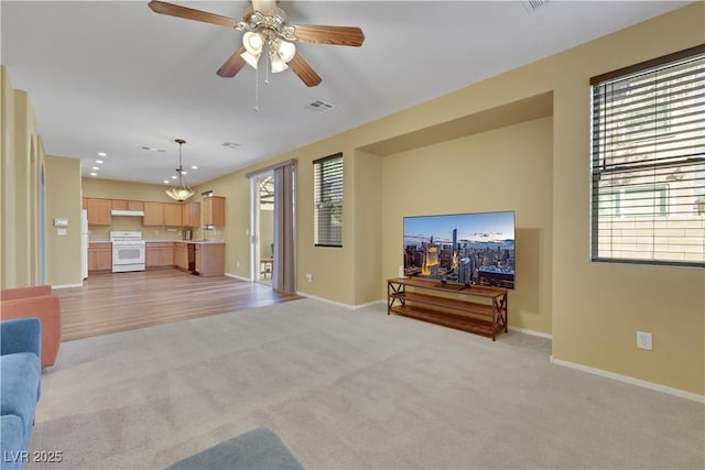 living area with light carpet, a ceiling fan, visible vents, and baseboards