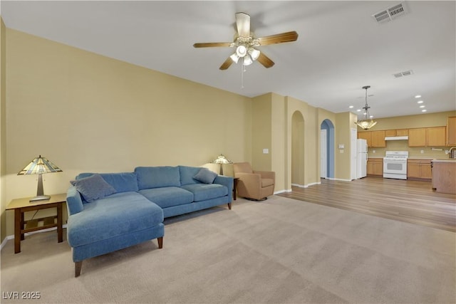 living area featuring arched walkways, visible vents, light carpet, and baseboards