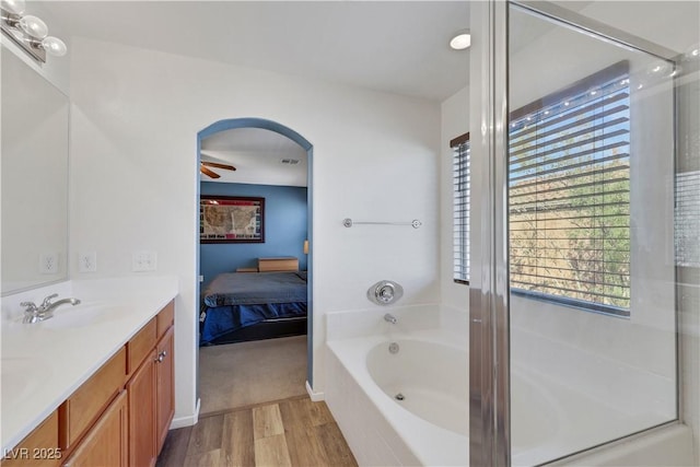 ensuite bathroom with ceiling fan, wood finished floors, vanity, a bath, and ensuite bath