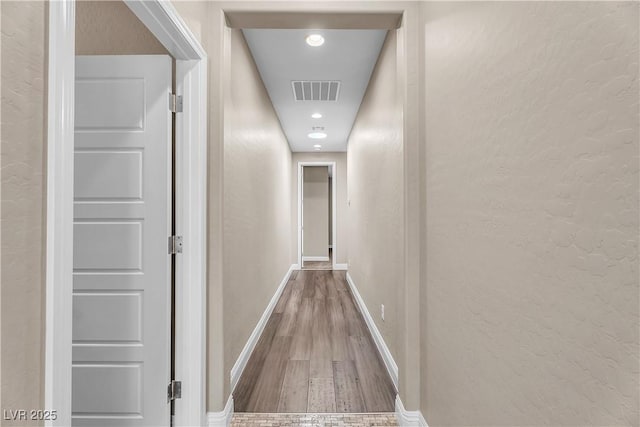 corridor featuring a textured wall, recessed lighting, wood finished floors, visible vents, and baseboards