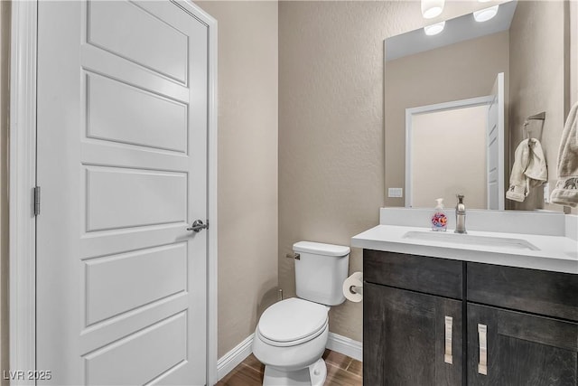 bathroom with a textured wall, toilet, wood finished floors, vanity, and baseboards