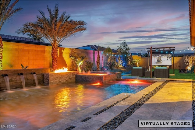 pool at dusk featuring an outdoor fire pit, a pool with connected hot tub, a patio area, and a fenced backyard