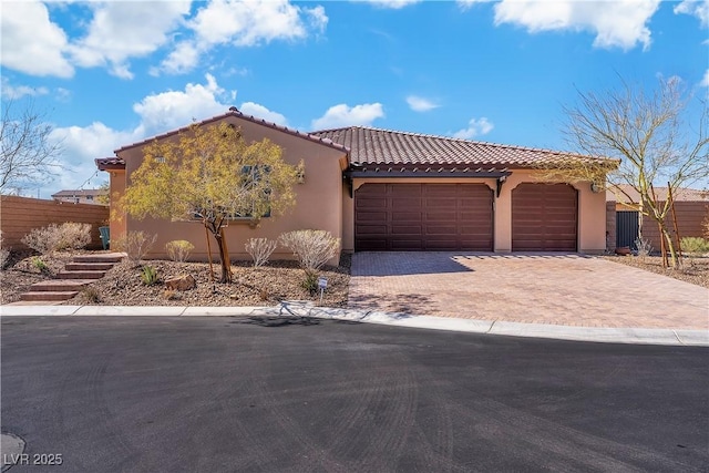 mediterranean / spanish-style home with decorative driveway, stucco siding, an attached garage, fence, and a tiled roof