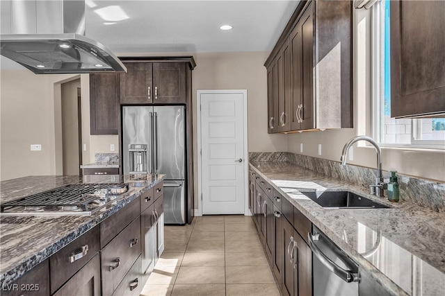 kitchen with light stone counters, island range hood, a sink, dark brown cabinets, and appliances with stainless steel finishes