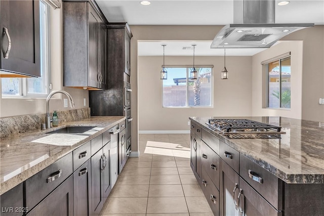 kitchen featuring appliances with stainless steel finishes, light stone countertops, island exhaust hood, dark brown cabinets, and a sink