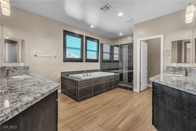 bathroom with a garden tub, a shower stall, visible vents, and a sink