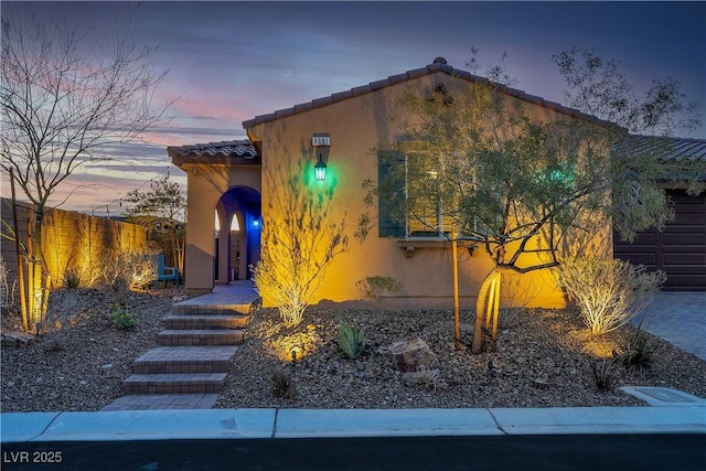 exterior space featuring a garage, fence, a tiled roof, and stucco siding