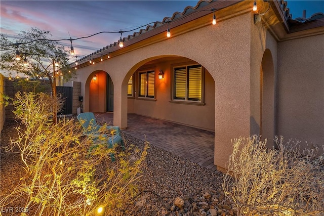 view of side of home with a patio, a tiled roof, and stucco siding