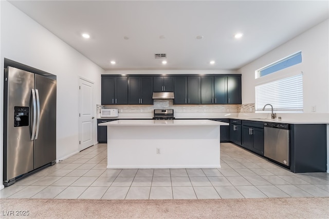 kitchen with under cabinet range hood, stainless steel appliances, a sink, light countertops, and a center island