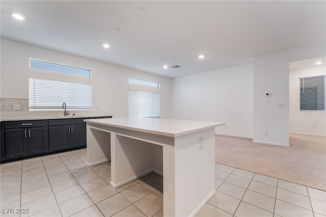 kitchen with light carpet, light tile patterned floors, a center island, light countertops, and a sink