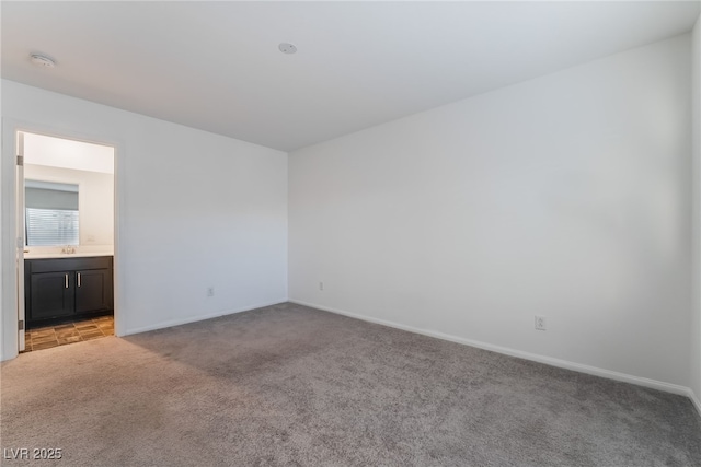 empty room featuring baseboards, a sink, and light colored carpet