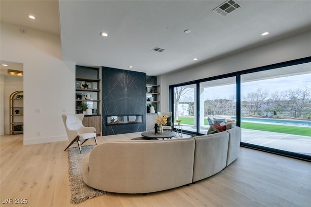 living area with built in shelves, visible vents, wood finished floors, and a high end fireplace