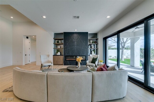 living room with built in shelves, visible vents, a fireplace, and light wood finished floors